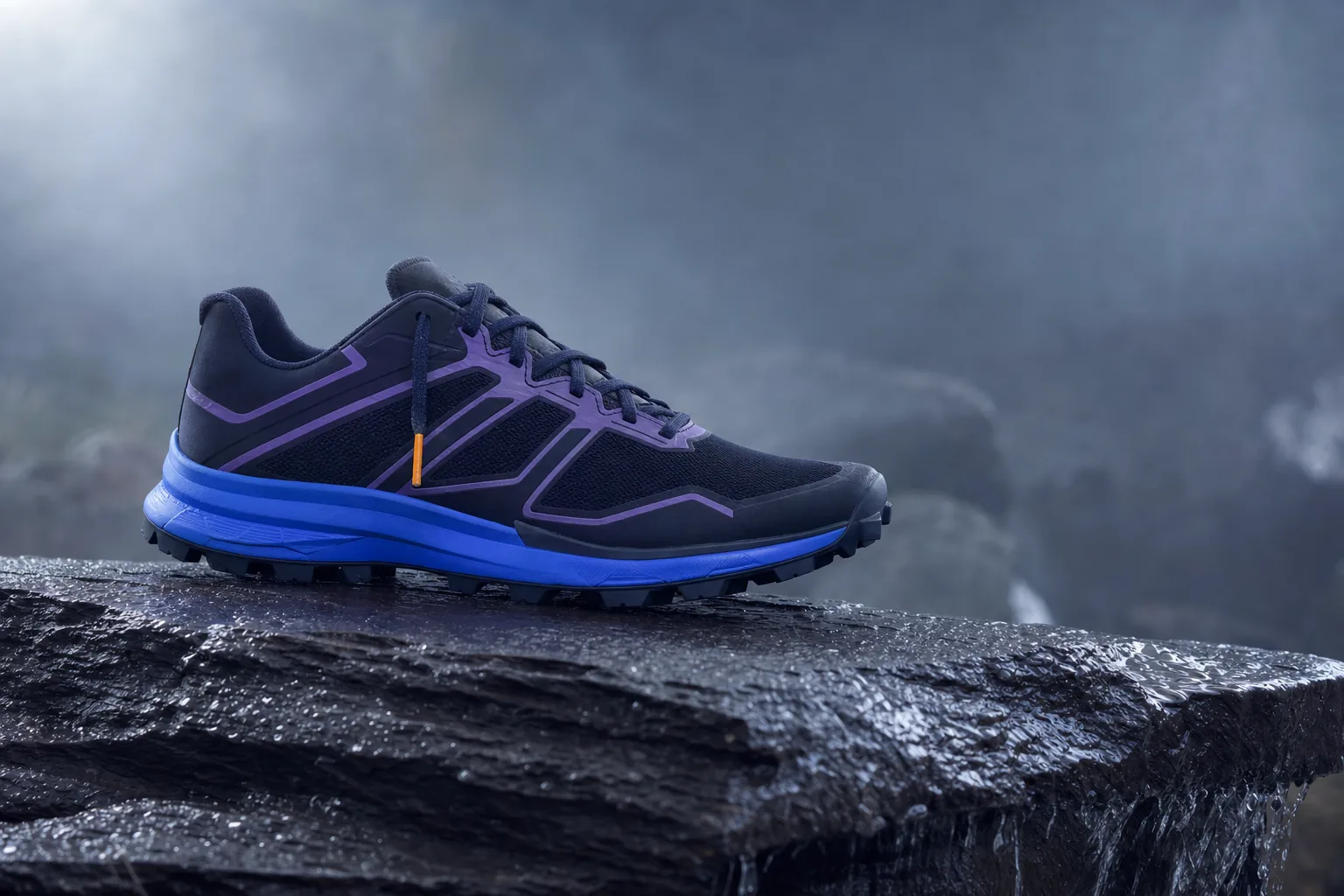 A single trail-running shoe in navy and electric blue planted on dark wet slate, water beading on the rock, one amber lace tip