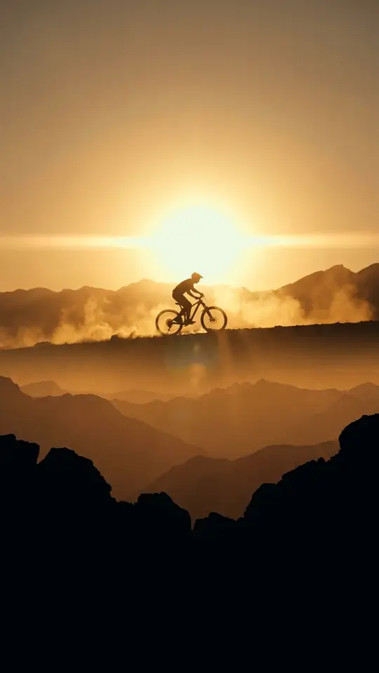 A rider silhouetted on a ridge against a huge low sun, dust glowing in the backlight